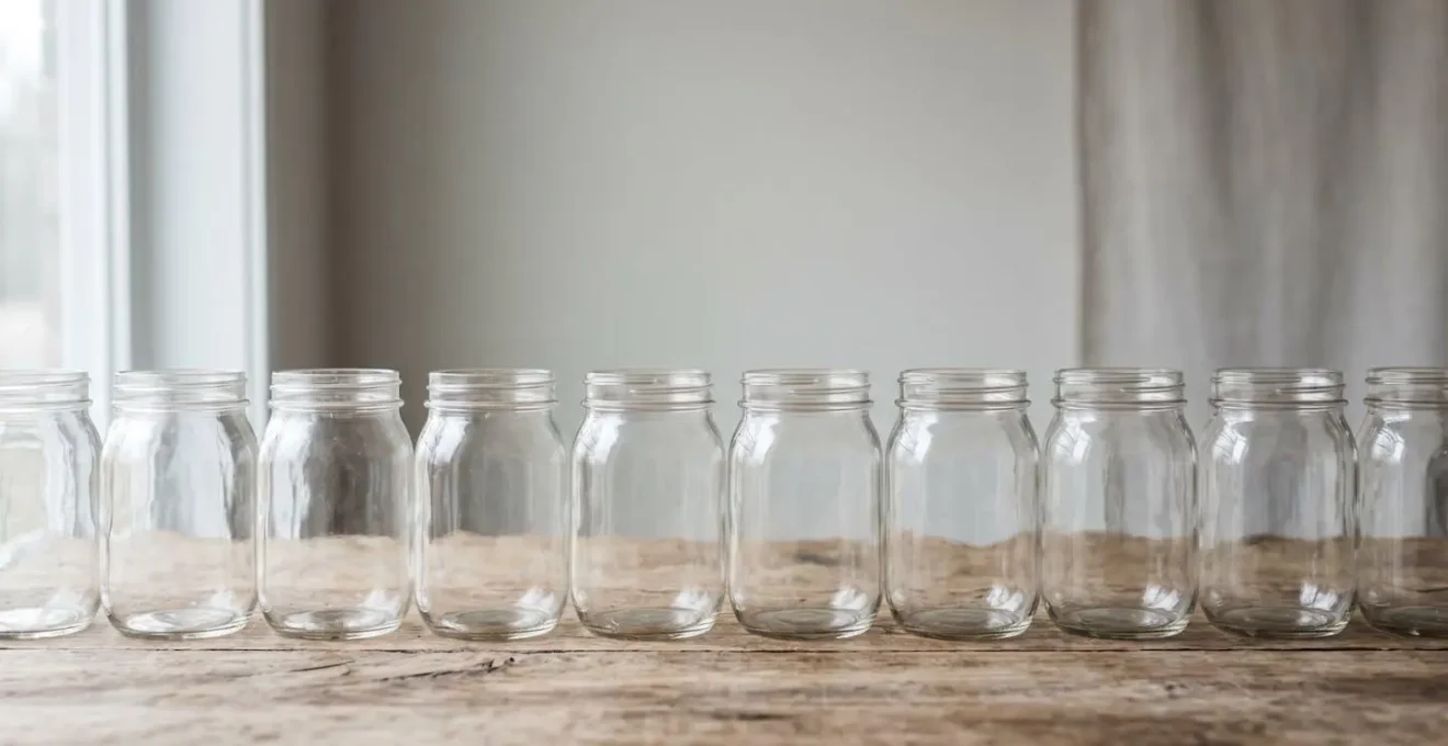 Vue d'ensemble minimaliste de bocaux en verre vides alignés sur une surface en bois brut dans une lumière naturelle