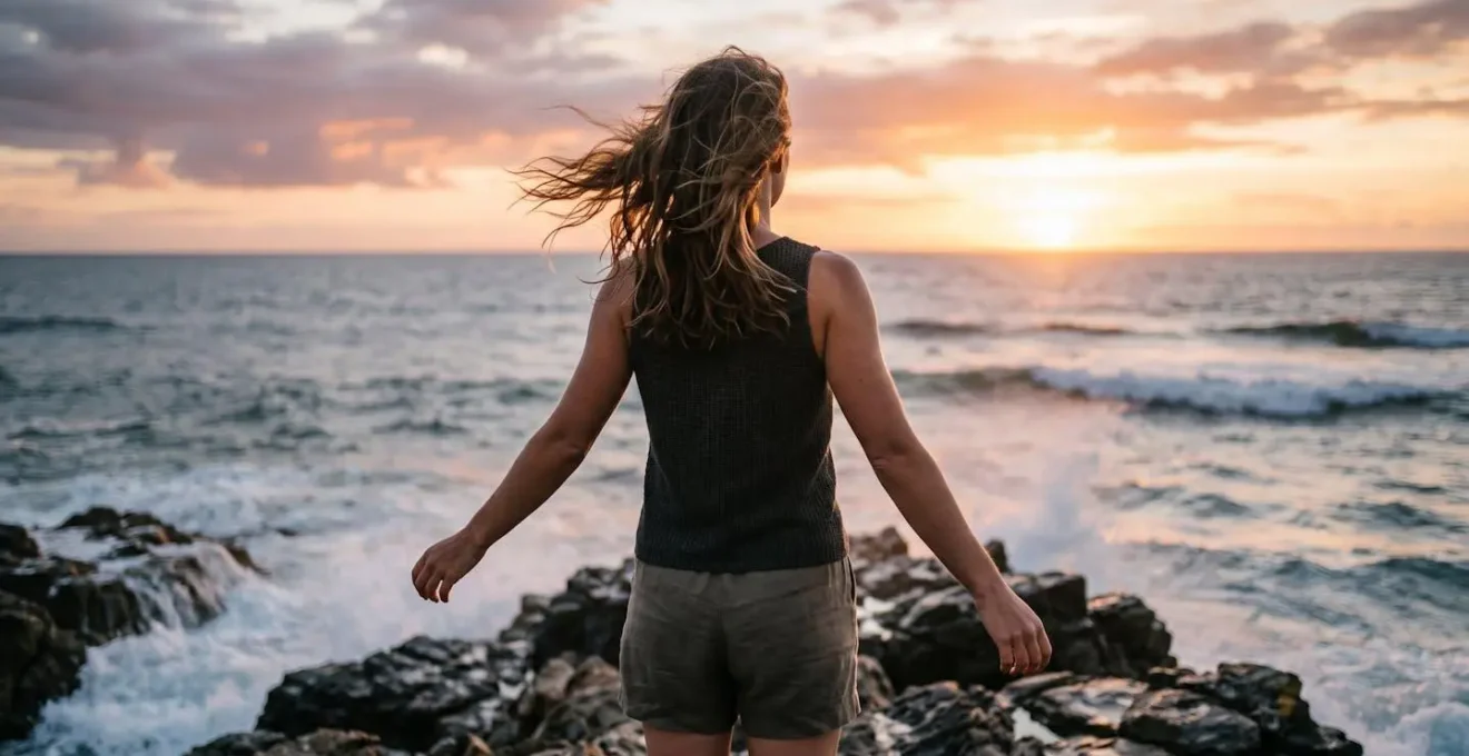 Personne de dos face au vent marin, peau dorée par le soleil couchant, cheveux au vent, illustrant la connexion directe avec les éléments naturels