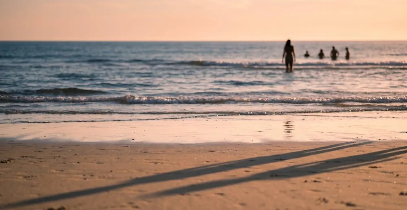 Scène minimaliste d'une plage en fin d'après-midi avec lumière dorée rasante, ombres longues et atmosphère sereine évoquant l'heure des habitués