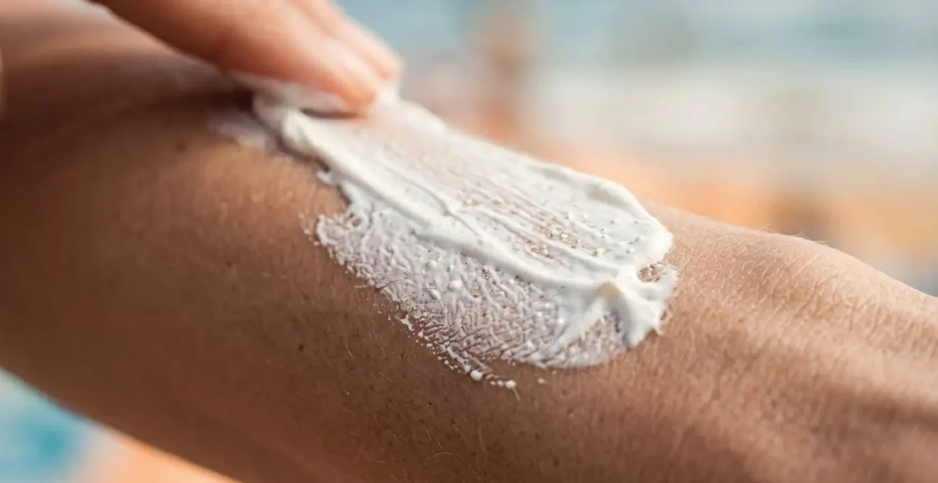 Gros plan macro sur l'application de crème solaire blanche sur une peau, texture crémeuse et détails de la peau visibles
