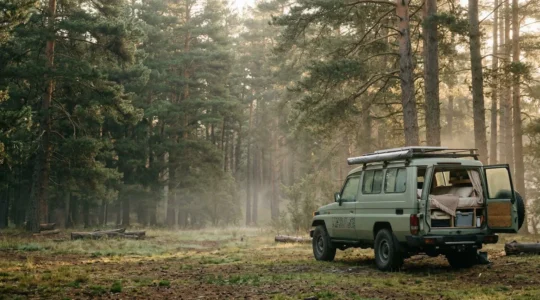 Vue large d'un véhicule aménagé garé dans un cadre naturel paisible au lever du soleil, évoquant la liberté du voyage naturiste